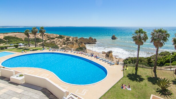 Une grande piscine incurvée offrant une vue sur l’océan et la côte rocheuse.