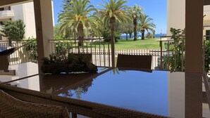 Un balcon doté d’une table en verre et de chaises en osier, donnant sur une pelouse bordée de palmiers et offrant une vue sur la mer.