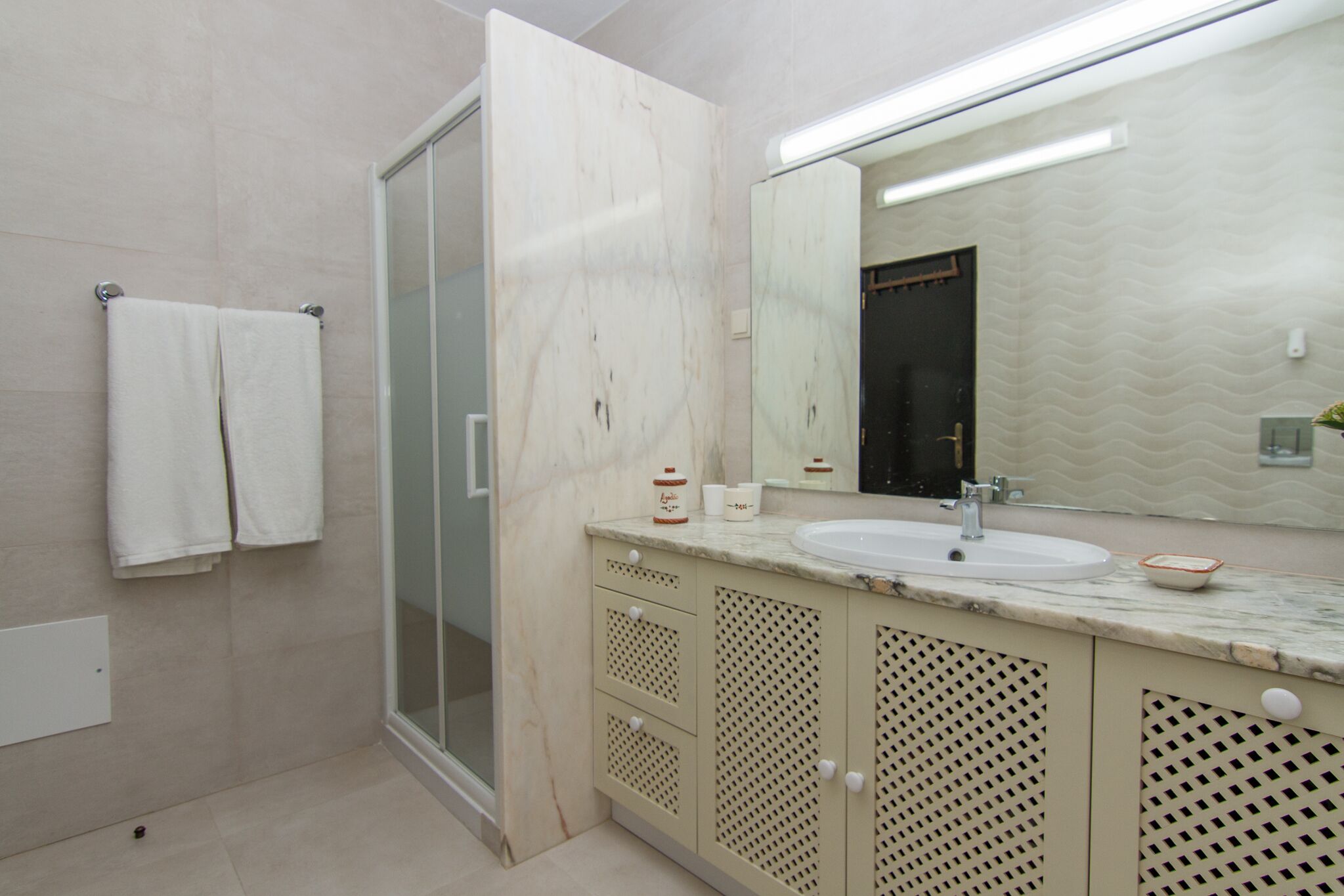 Ein Badezimmer mit Glastrennwand zur Dusche, einem Waschbecken mit Marmorplatte und einem großen Spiegel.