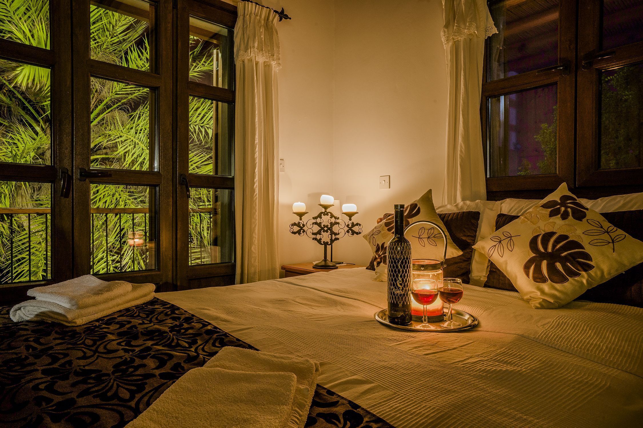 A well-lit bedroom with a bed, a bedside table with a candle, and a window with curtains.