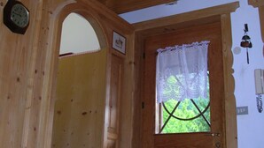 Un intérieur en bois avec une porte, une fenêtre ornée de rideaux en dentelle et une horloge au mur.