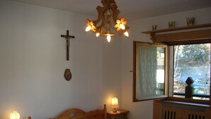 Une chambre à coucher avec un lit en bois, deux tables de chevet avec des lampes, une croix accrochée au mur et une fenêtre donnant sur l’extérieur.
