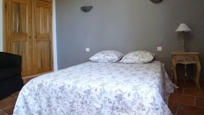Ein Schlafzimmer mit einem Bett, zwei Kissen, einem Nachttisch mit Lampe, einem Holzschrank und einem Sessel.