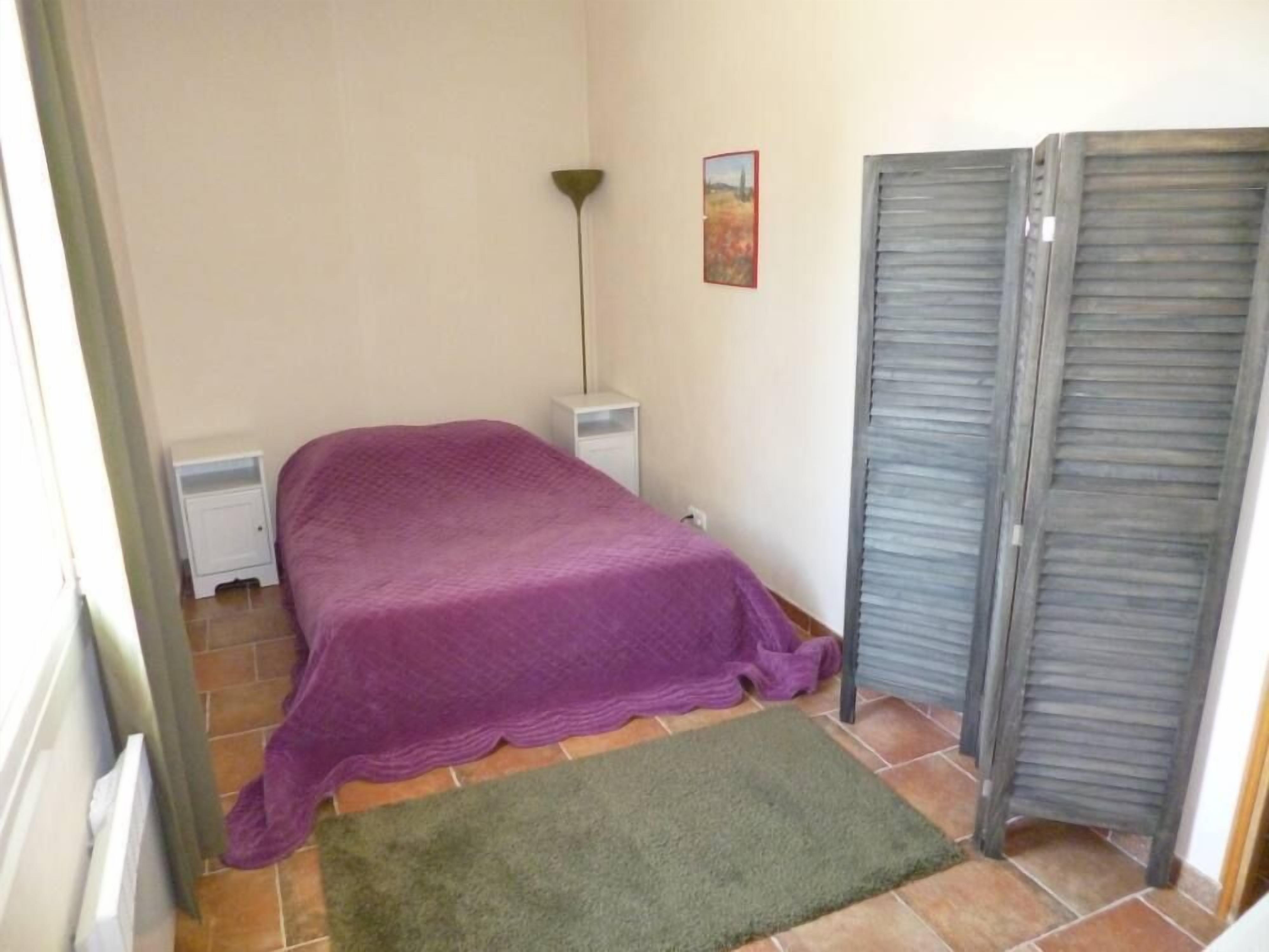 Ein kleines Schlafzimmer mit einem Bett, einem Nachttisch, einer Lampe, einem Bild an der Wand und einer Schiebetür.