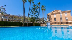Una piscina cristallina di colore blu circondata da alte palme, con un edificio sullo sfondo.