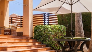 Una zona patio con tavolo e sedie, un ombrellone grande e una scalinata che conduce a un pontile di legno.