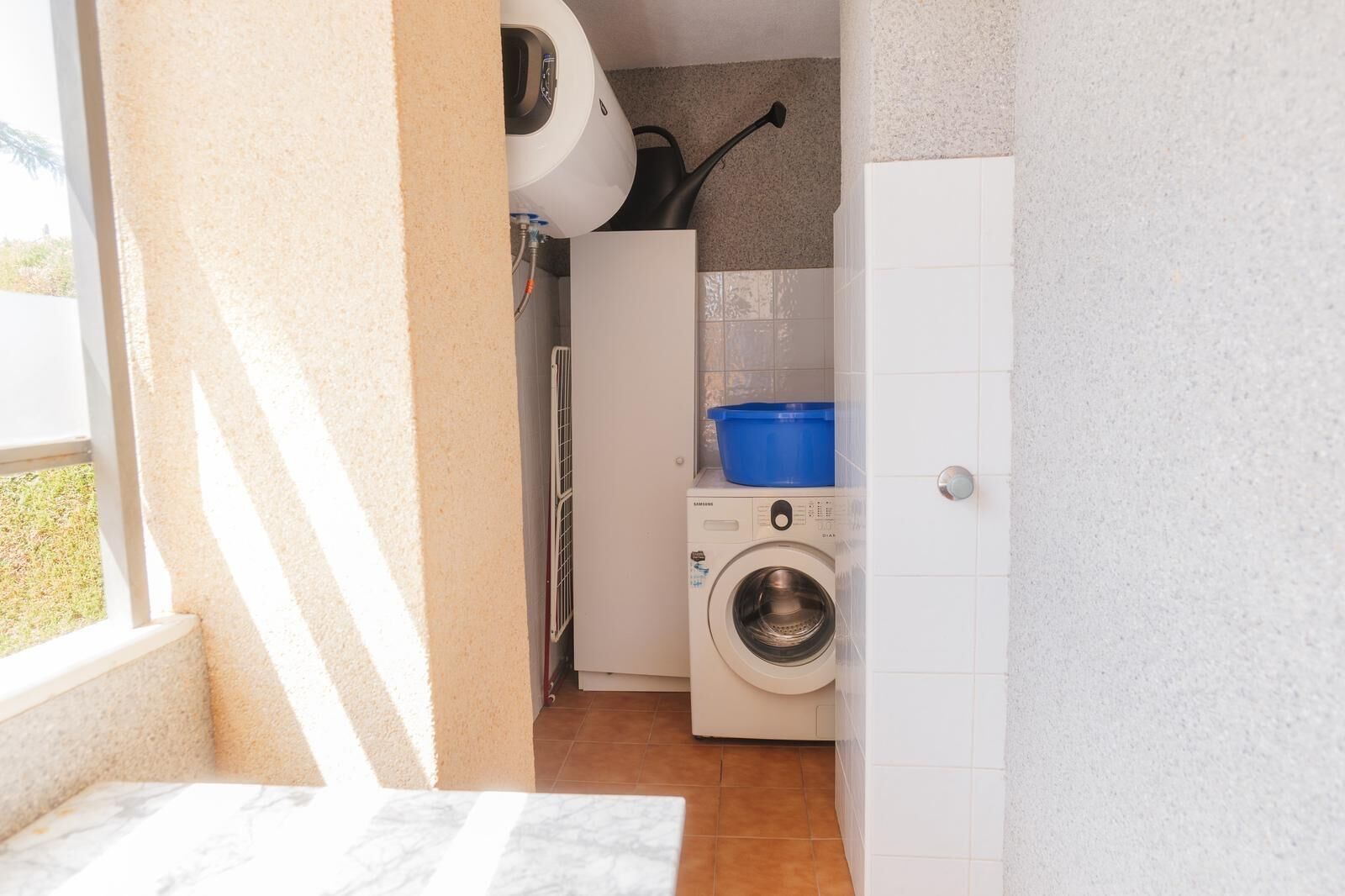 A compact laundry room with a washing machine, a drying rack, and a blue basin on a shelf.