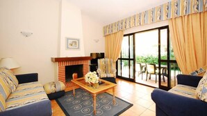 Una sala de estar con chimenea, dos sofás, una mesa de centro y vistas a un área exterior a través de puertas de vidrio grandes.
