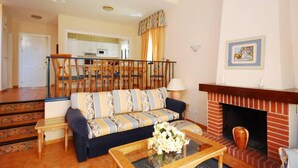 Una sala de estar con sofá, mesa de centro, chimenea y una escalera que lleva a la cocina.