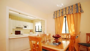 Un comedor con una mesa y sillas de madera, una cocina con armarios blancos y una ventana con cortinas.