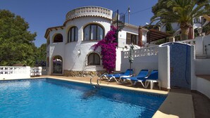 A pool area with a white building, blue lounge chairs, and a palm tree.
