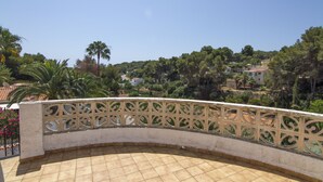 A curved balcony with a decorative metal railing, overlooking a residential area with houses and trees.