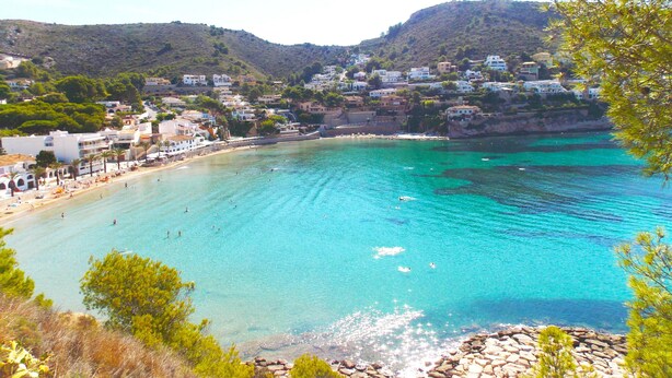 A coastal town with clear turquoise waters, white buildings, and a rocky shoreline.