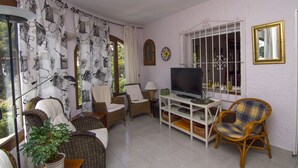 A living room with wicker furniture, a television, and a window with decorative iron bars.