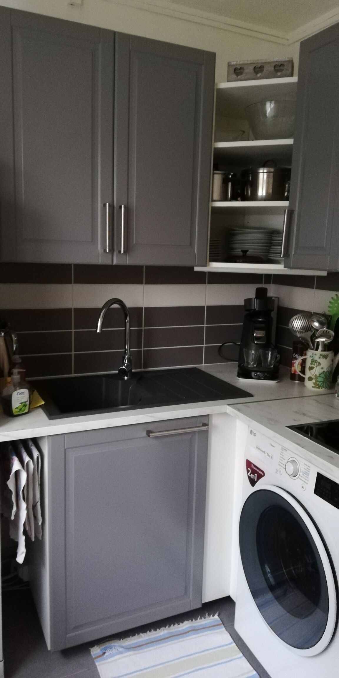 A compact kitchen with grey cabinets, a stainless steel sink, a coffee maker, and a front-loading washing machine.