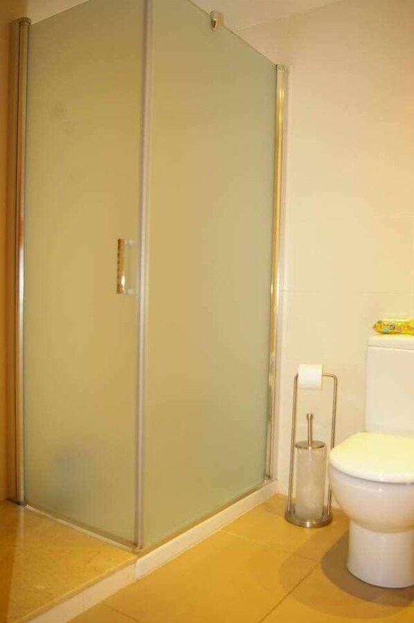 A bathroom with a glass shower enclosure, a toilet, and a paper towel dispenser.