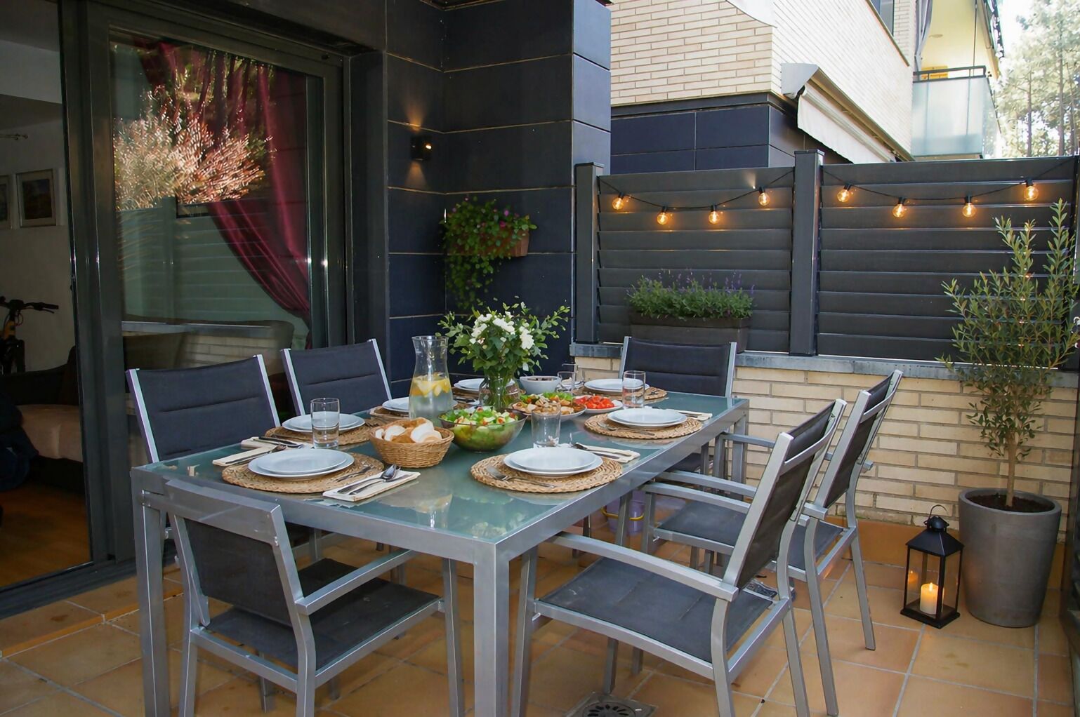 Ulkoterassi, jossa on lasipöytä, metallituolit ja monenlaisia ruokalajeja.
