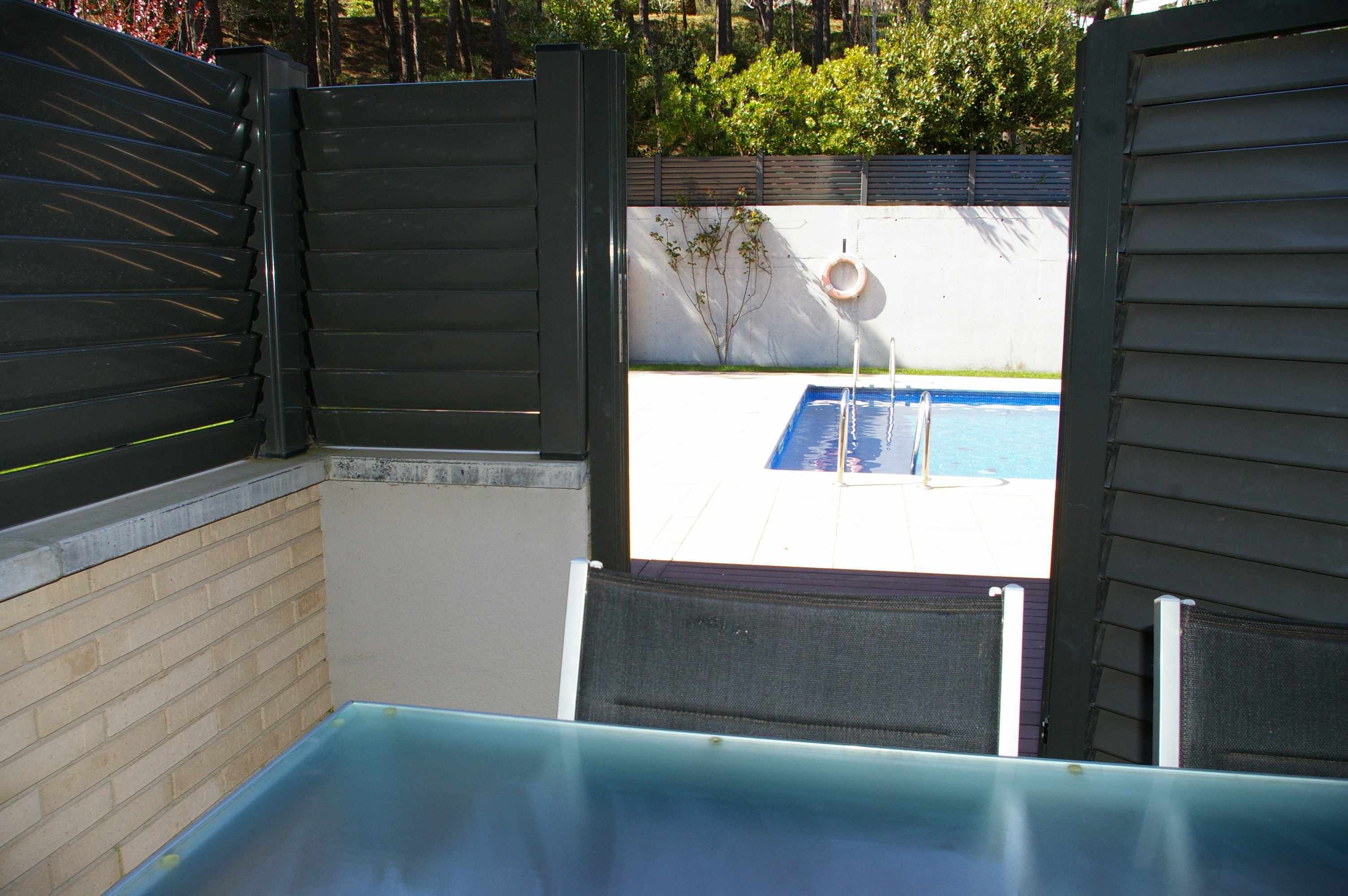 Un espace piscine avec vue à travers une porte entrouverte, une chaise au bord de la piscine et un tuyau d’arrosage.