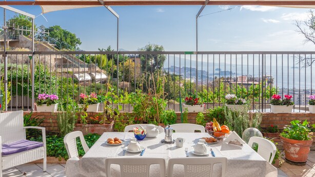 An outdoor dining area with a table set for two, surrounded by potted plants and a view of the cityscape. - Sea View 2bed Apartment overlooking the Gulf with Private Terrace (Napoli)