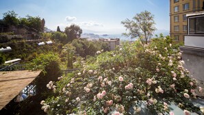 A rooftop garden with lush pink roses, a wooden deck, and a view of the cityscape and mountains in the distance. - Sea View 2bed Apartment overlooking the Gulf with Private Terrace (Napoli)