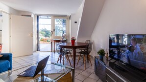 A modern living room with a glass coffee table, a laptop, a TV, and a dining area with chairs and a table. - Sea View 2bed Apartment overlooking the Gulf with Private Terrace (Napoli)