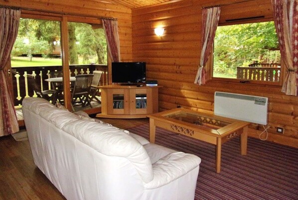 A log cabin interior with a white sofa, a wooden table, a television, and a cabinet.