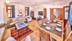 Amplia sala de estar con un sofá, una mesa de comedor para cuatro personas, un televisor y una estantería.