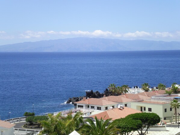 A coastal building with a red-tiled roof, white walls, and a balcony overlooking the sea.