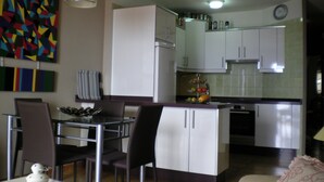 A modern kitchen with white cabinets, a refrigerator, and a fruit display. There is a dining area with chairs and a table. - Tenerife, La Arena Beach 300 m away, free Wi-Fi, community pool (Santiago del Teide)