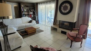 A living room with a sofa, armchair, and a fireplace. There is a bookshelf and a clock on the wall. - 70m from the beach, pretty house 200m2, sea view, 6 bedrooms, 5 bathrooms, 7 wc, enclosed garden, 15 people (Poggio-Mezzana)
