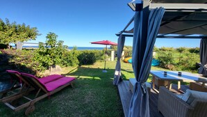 A covered outdoor seating area with a view of the sea, a wooden bench, and a table with cushions. - 70m from the beach, pretty house 200m2, sea view, 6 bedrooms, 5 bathrooms, 7 wc, enclosed garden, 15 people (Poggio-Mezzana)