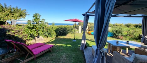Ein überdachter Außenbereich zum Sitzen mit Meerblick, einer Holzbank und einem Tisch mit Kissen.