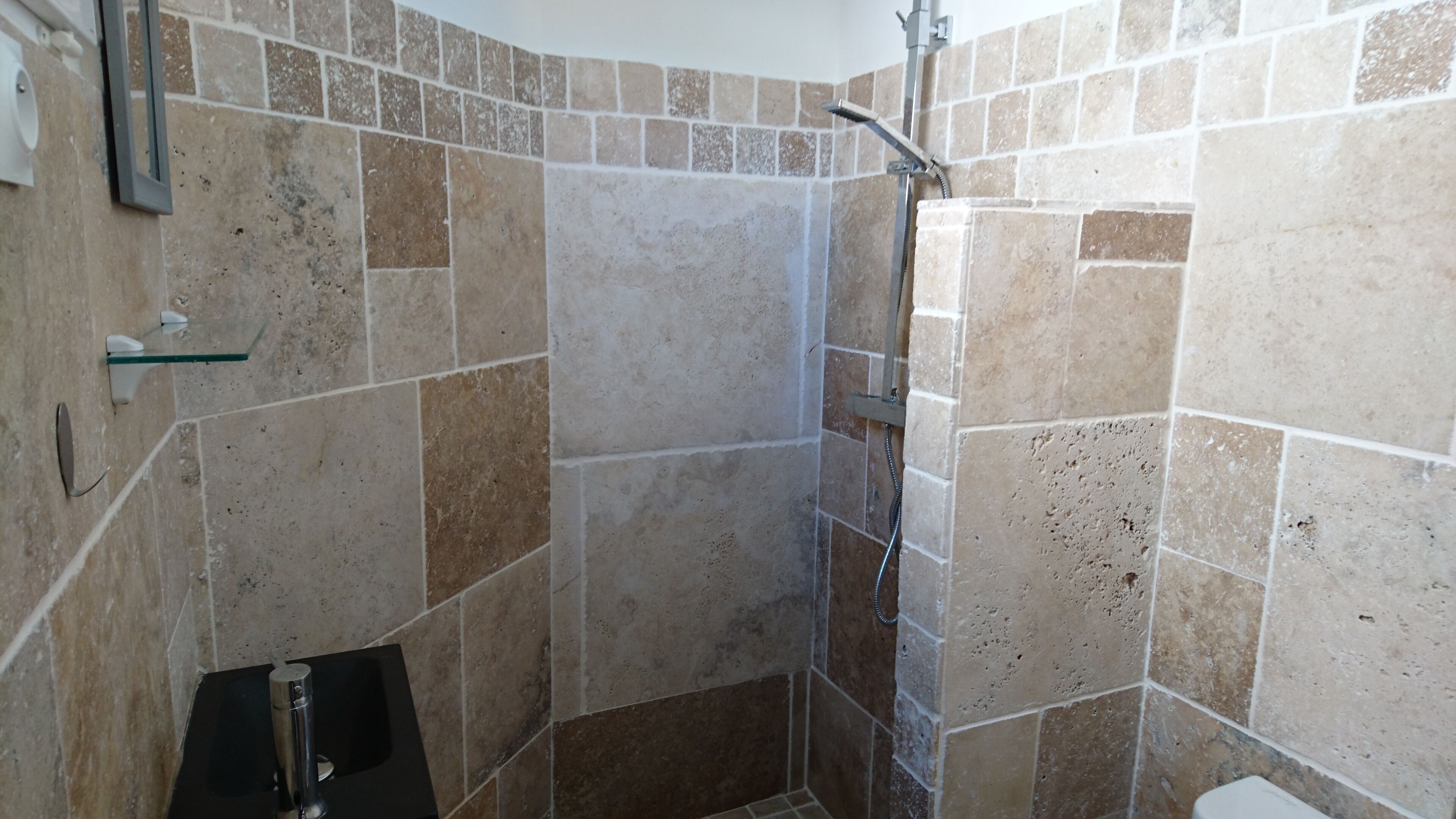 Ein Duschbereich mit einer Glasablage, einem schwarzen Waschbecken und einer gefliesten Wand.