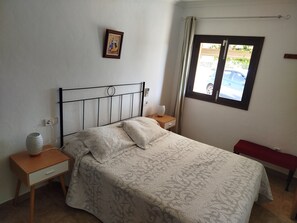 A neatly made bed with a patterned bedspread, a bedside table with a vase, a wall-mounted picture, and a window with a view of the outside. - ideal place to relax and unwind farm. (Santa Margalida)