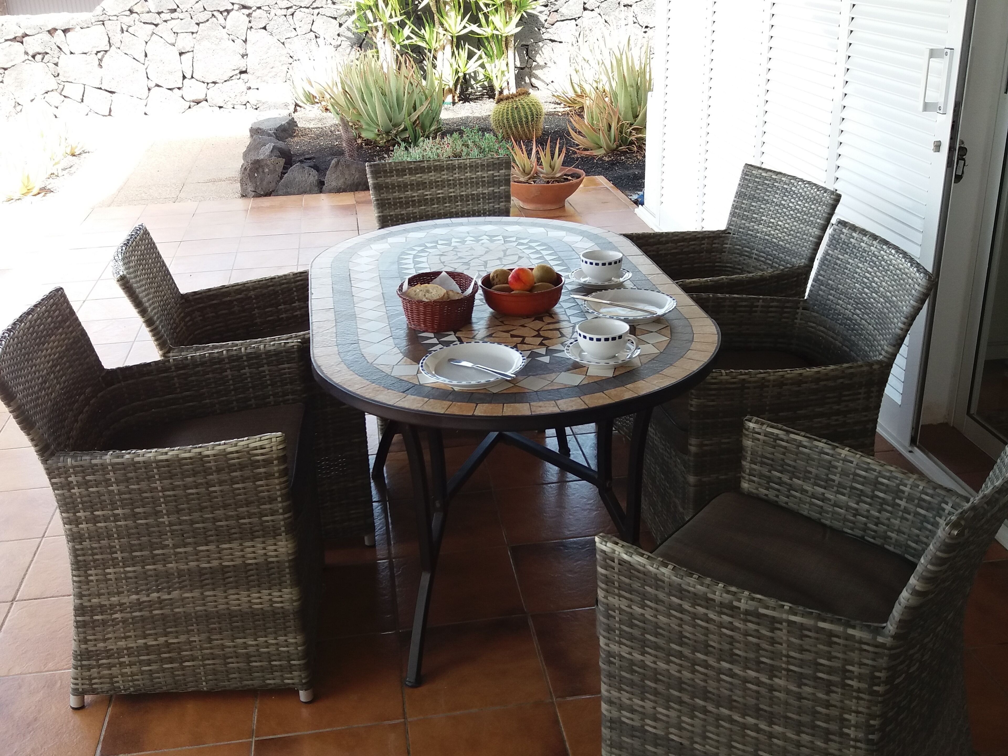 A round table with a mosaic top surrounded by wicker chairs.