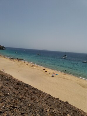 A beach with clear turquoise water, a sandy shore, and several boats in the distance.