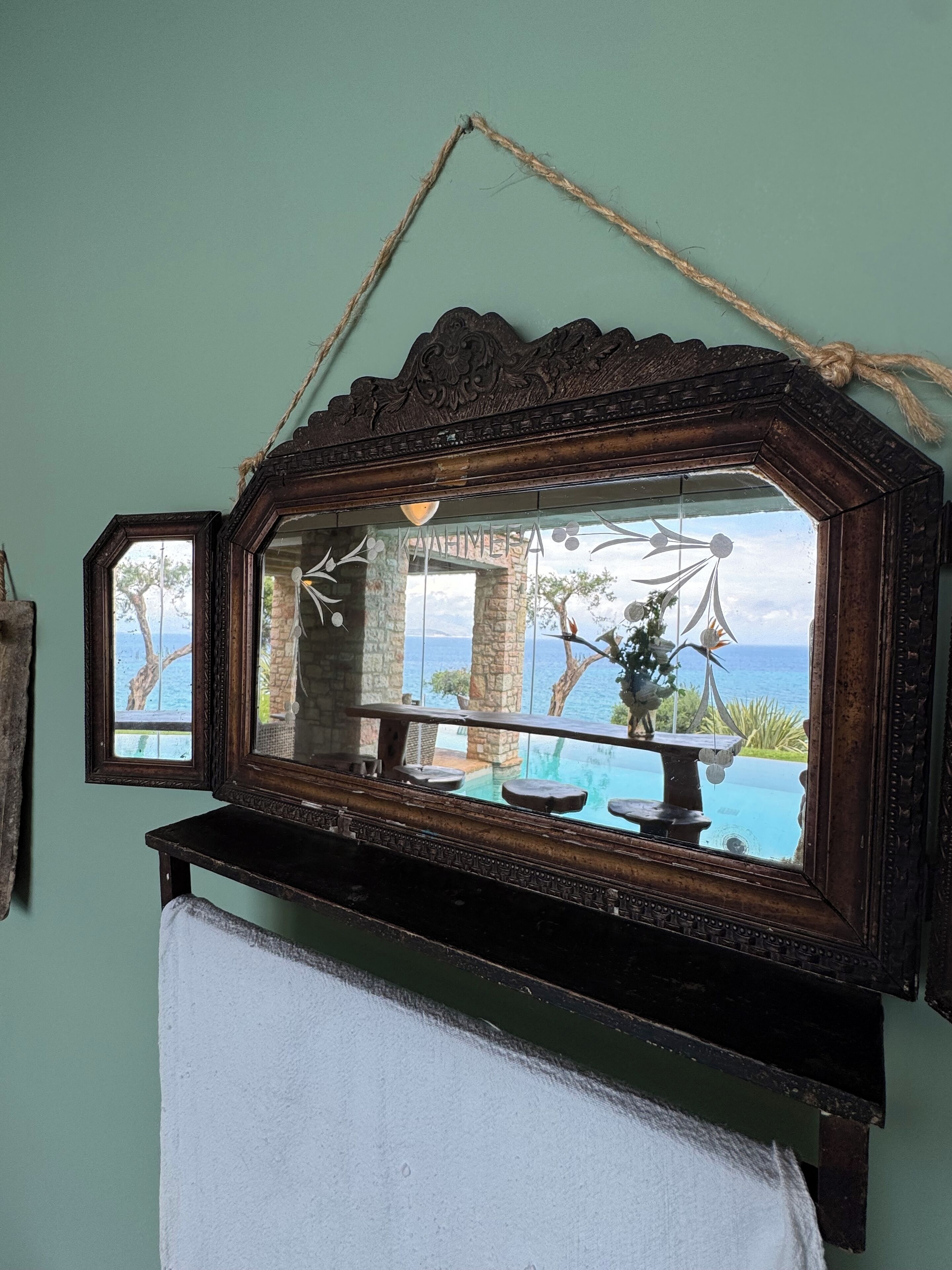 A mirror with a rustic frame, a towel, and a view of an outdoor pool and landscape.