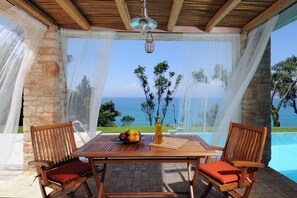 A wooden table with a fruit bowl, a bottle, and a glass, set against a stone wall with a view of the sea. - Villa Seashore: Dreamy villa by the sea side with heated pool (Corfu)