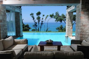 A poolside area with a view of the sea, stone pillars, and wicker furniture. - Villa Seashore: Dreamy villa by the sea side with heated pool (Corfu)