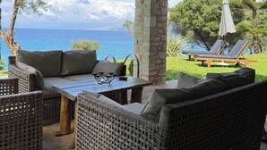 Un espacio de estar al aire libre cubierto con mobiliario de mimbre, una mesa y vista al mar.