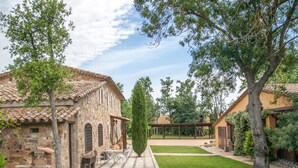 A stone building with a tiled roof, a patio with outdoor seating, and a well-maintained lawn.