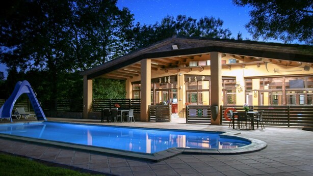 A covered outdoor pool area with a seating area and a building with large windows.