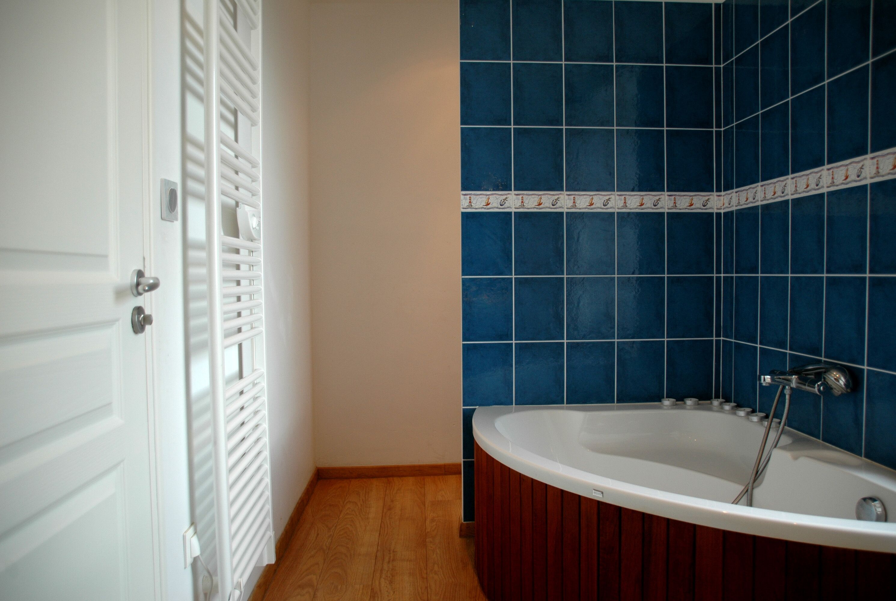 A bathroom with a white bathtub, blue tiled walls, and a wooden floor.