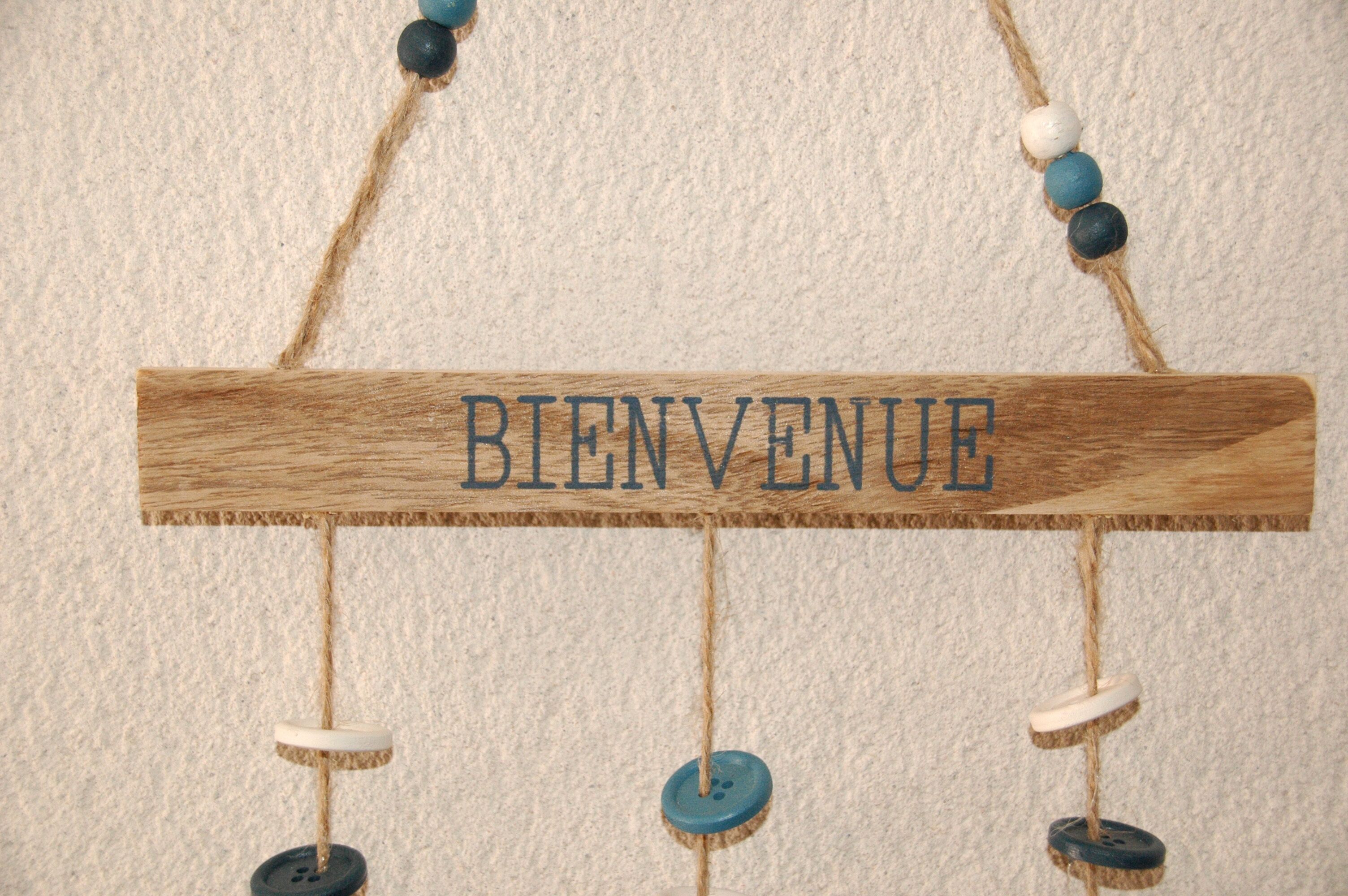 Un cartello di legno con la scritta “BIENVENUE” appeso a un filo con dei bottoni.
