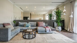 Een moderne woonkamer met een grijze modulaire bank, een ronde salontafel en een grote potplant.
