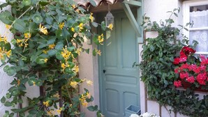 A house with a green door, a window with a white frame, and a wall with green foliage and red flowers. - Air-Conditioned Cottage With Pool in Vence. (Vence)