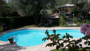 A swimming pool with a tiled edge, surrounded by a garden with various plants and a gazebo in the background. - Air-Conditioned Cottage With Pool in Vence. (Vence)