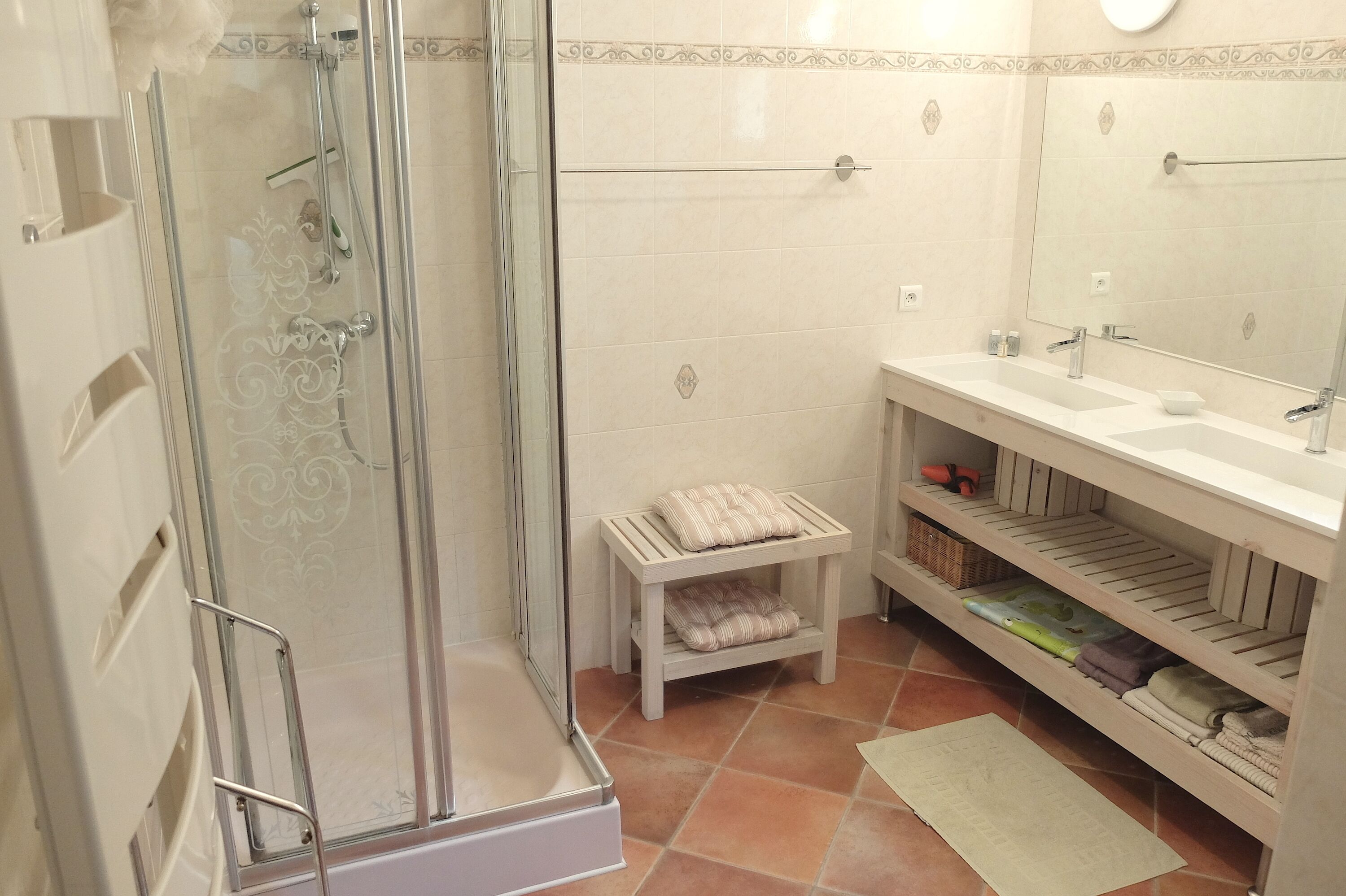 Un baño con ducha de vidrio, tocador con espejo y repisas con toallas dobladas.