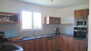 A kitchen with wooden cabinets, a built-in microwave, an oven, a sink, and a window with a view of greenery outside. - House / Villa - Saint Pée sur Nivelle (Saint-Pée-Sur-Nivelle)