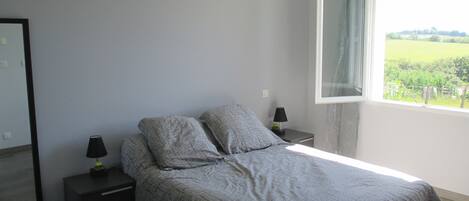 A bedroom with a bed, two bedside tables, a mirror, and a window with a view of greenery.